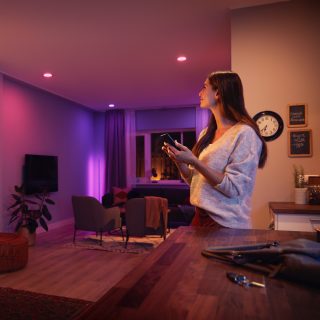 Person adjusting smart lighting with a mobile device in a modern living room with colored lights illuminating the space.