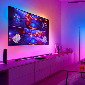 Un juego de carreras aparece en una gran pantalla de televisión colgada en una pared con IluminaciÃ³n envolvente sincronizada a su alrededor.