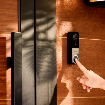 Un dedo pulsando el botón de un videoportero con cable instalado en una pared