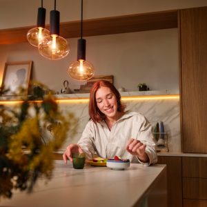 Une femme qui mange à table avec des lampes Hue au-dessus d’elle et une bande lumineuse derrière elle.