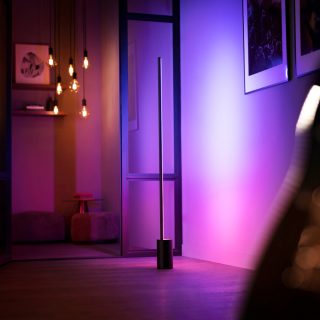 Un lampadaire dégradé Signe projetant une lumière intelligente rose et violette contre un mur.