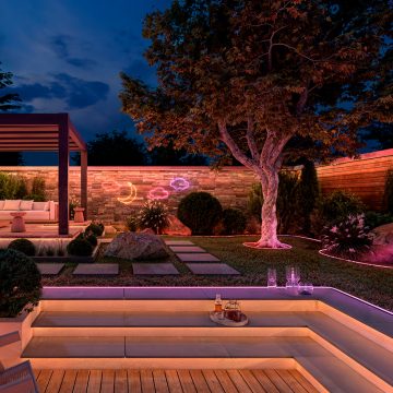 Un jardin et une terrasse éclairés dans des tons doux de jaune, de rose et de violet provenant de lightstrips dissimulés sous les marches et de lightstrips visibles le long des parterres de fleurs et sur les murs. 