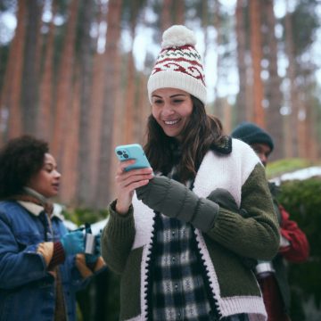 Une femme souriante vérifie son système de sécurité de maison connecté sur un smartphone dans une forêt