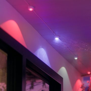 Una striscia di luci permanenti Festavia attaccata al soffitto di un balcone con moduli luminosi che emettono luce rosa e viola