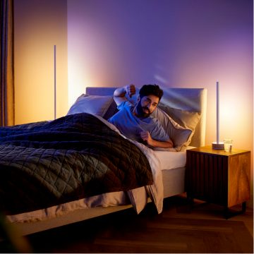 Man rekt zich uit in bed met zacht verlichte slimme vloer- en tafellampen 