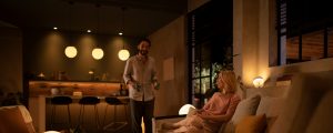 Een stel in een woonkamer geniet tevreden van de warmwitte tinten van slimme verlichting, ter aankondiging van de Philips Hue nieuwjaarsdeals.