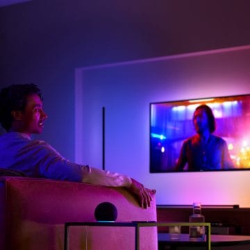 Man die op de bank tv kijkt met surroundverlichting en een slimme speaker op de bijzettafel naast hem