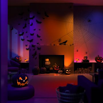 Gekleurde, slimme Philips Hue lampen, verspreid over een voor halloween versierde woonkamer, met gloeiende oranje pompoenen.