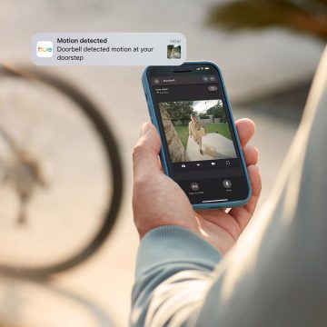 En person overvåker inngangsdøra si med en Hue Secure Video Doorbell via Hue appen mens de er borte fra hjemmet. 
