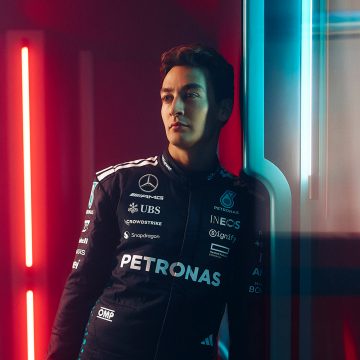 F1-fører George Russell sitter på en beige sofa i en stue med myk, varm belysning.