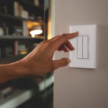 Mão prestes a ligar um interruptor de luz inteligente branco na parede