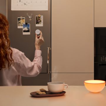 Kvinna placerar en Hue Smart button (av senaste modell) på kylskåpet med dess magnetfäste.